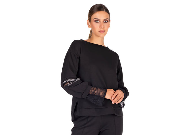 Woman wearing a black outfit with lace details on sleeves against a white background