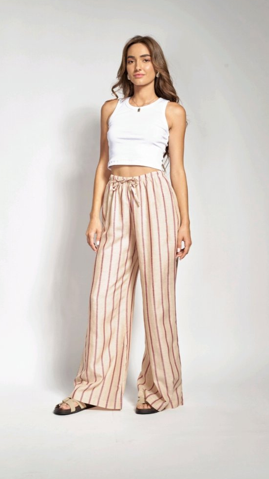 Woman wearing a white top and striped pants standing against a plain background